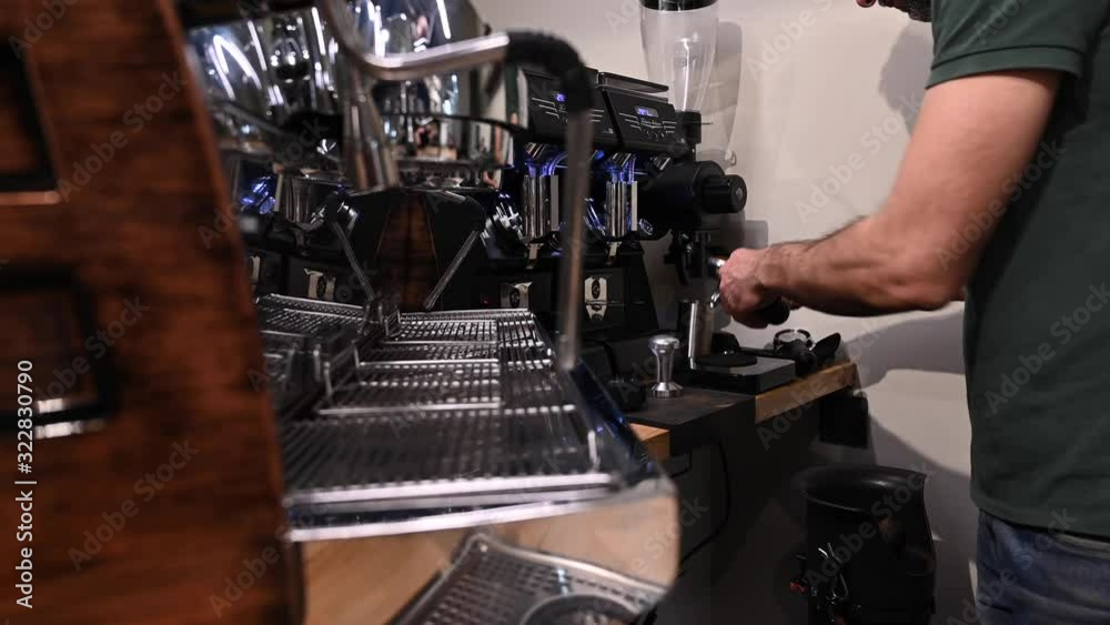 Close-up shot of barista holding filter holder while coffee machine brewing fresh espresso into glass
