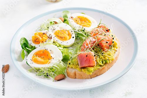 Breakfast. Healthy open sandwich on toast with avocado and salmon, boiled eggs, herbs, chia seeds on white plate with copy space. Healthy protein food.