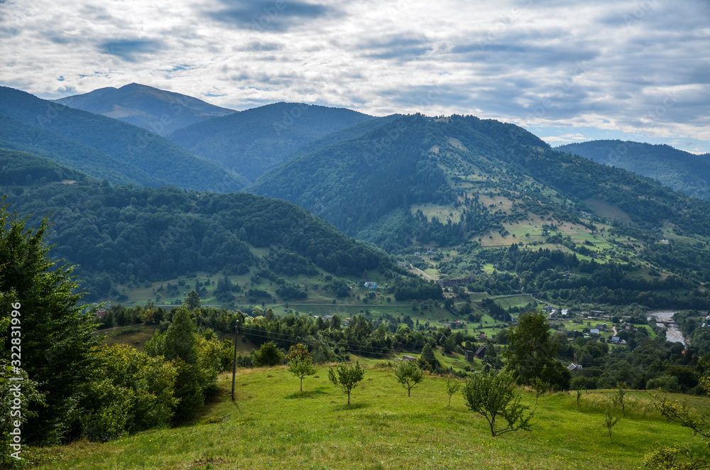 Beautiful panorama of the Carpathian village against backdrop of scenic mountains, where the highlanders live Hutsul. Wild forests, fields pastures, Ukraine 