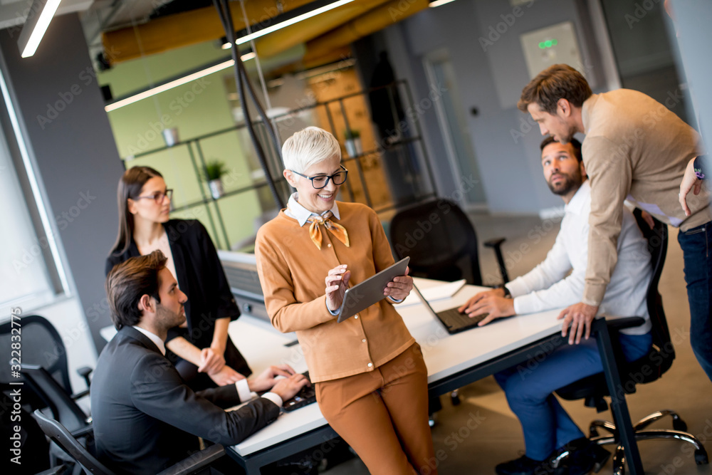 Business people working and communicating while standing in the office together with colleagues sitting in the background Business people working and communicating while standing in the office together with colleagues sitting in the background