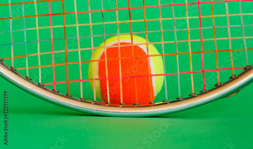 a racket and a tennis ball/ the oval of a tennis racket metal with strings of many colors and a tennis ball yellow and orange
