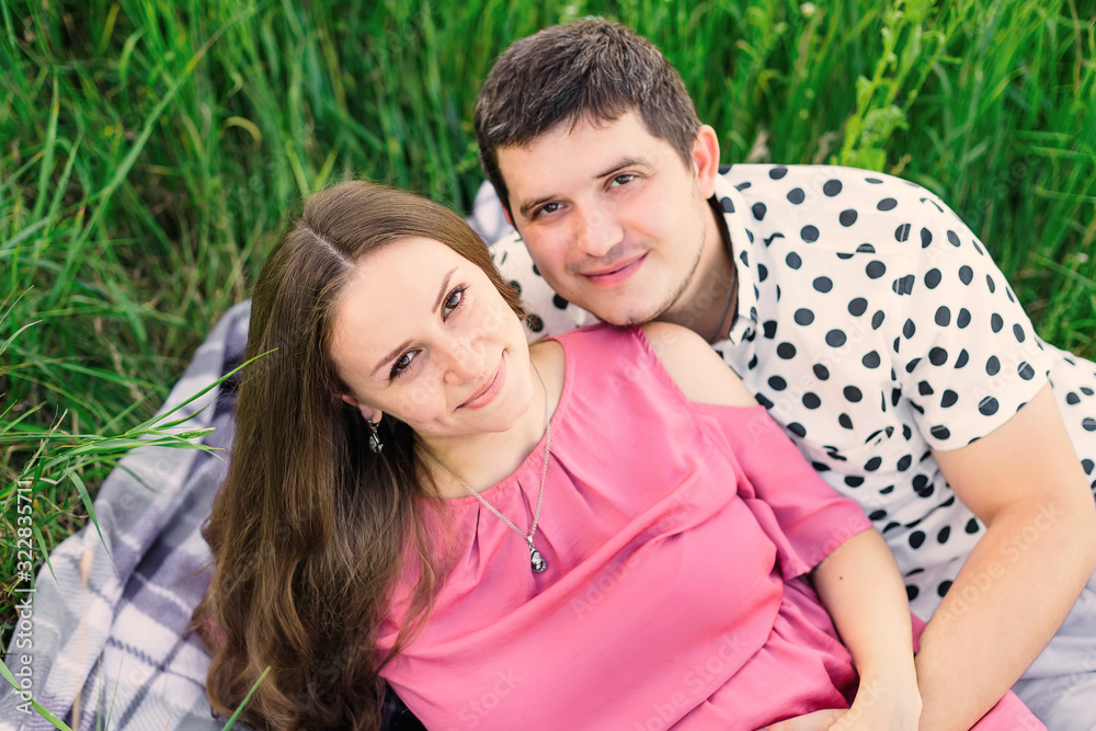 expectant parents looking at the camera and lying on the grass.