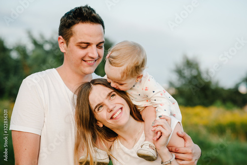 Portrait of a happy young family spending time together on nature, on vacation, outdoors. Mom, dad holds daughter stand on the grass. The concept of family holiday.