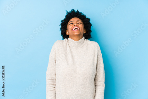 Middle aged african american woman against a blue background isolated laughs and closes eyes, feels relaxed and happy. © Asier