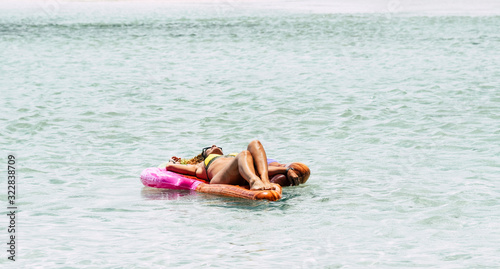Happy and relaxed woman with bikini lay down on a coloured lilo at the beach enjoying the blue transparent amazing water in summer holiday travel vacation lifestyle