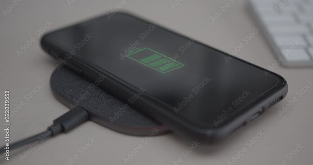Close up of Smart Phone battery being charged on wireless charger on desk