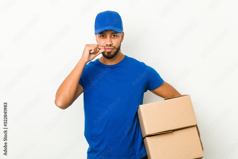 Young south-asian delivery man with fingers on lips keeping a secret. Young south-asian delivery man with fingers on lips keeping a secret.
