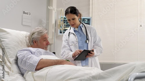 female doctor talking with a mature senior patient on the hospital bed showing to him medical results test on tablet comptur device photo