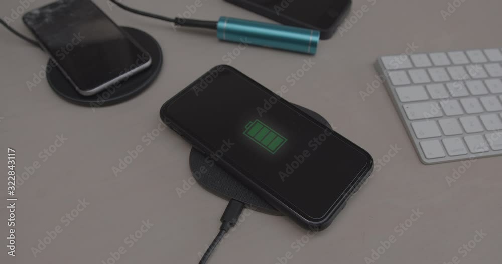Close up of Smart Phone battery being charged on wireless charger on desk Close up of Smart Phone battery being charged on wireless charger on desk