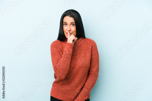 Young caucasian woman isolated on a blue background keeping a secret or asking for silence. © Asier