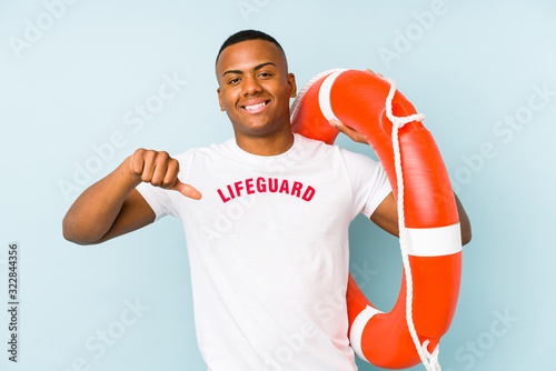 Young latin life guard isolated on blue background showing a dislike gesture, thumbs down. Disagreement concept. © Asier