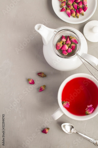 Herbal tea with pink roses in the white cup on the grey concrete background. Top view. Location vertical. Copy space.