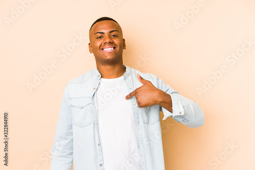 Young latin man isolated on beige background person pointing by hand to a shirt copy space, proud and confident