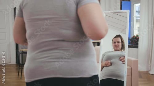 Overweight girl checking skin in front of mirror, looking at cellulite on body photo