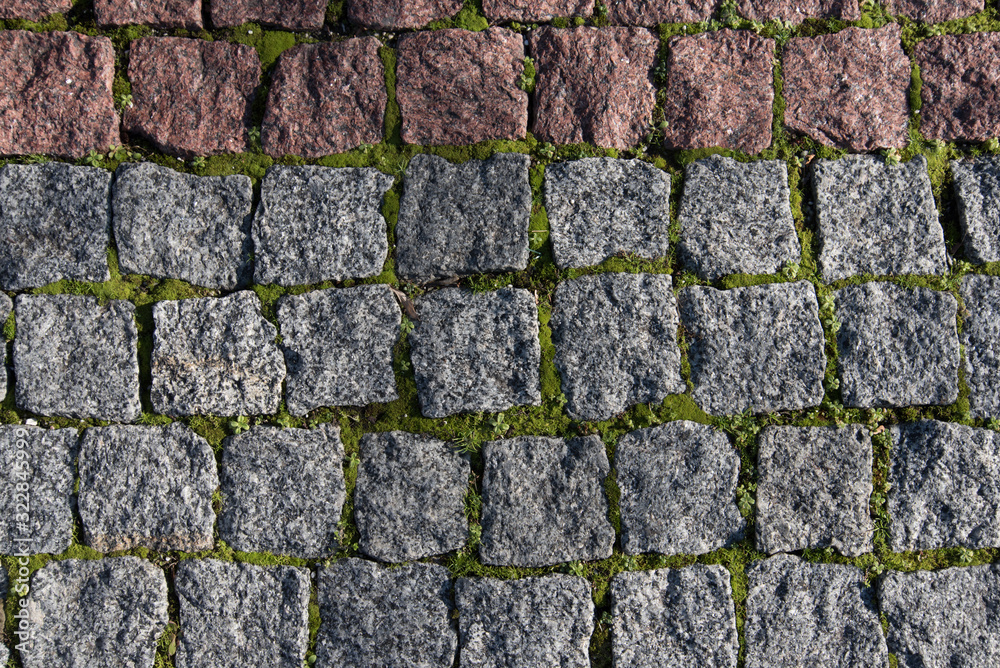 Obraz premium Paving stones made of natural stone. Paths for pedestrians. Beautiful square-shaped stones. Grass breaks through the rocks. The view from the top.