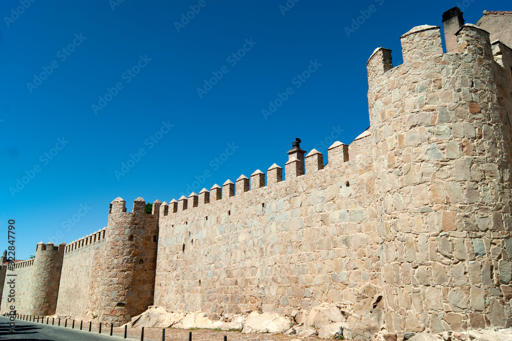 The defensive walls at the Spanish medieval city of Avila. Defensive battlements set against a blue summer sky in the heart of Spain / copy space.