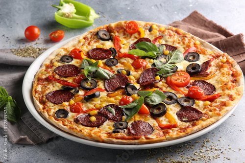 The concept of Italian cuisine. Pepperoni pizza with tomatoes, basil, corn and olives on a light background. Background image, copy space