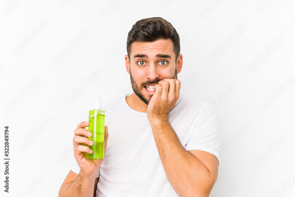 Young caucasian man holding a moisturizer with aloe vera isolated biting fingernails, nervous and very anxious. Young caucasian man holding a moisturizer with aloe vera isolated biting fingernails, nervous and very anxious.