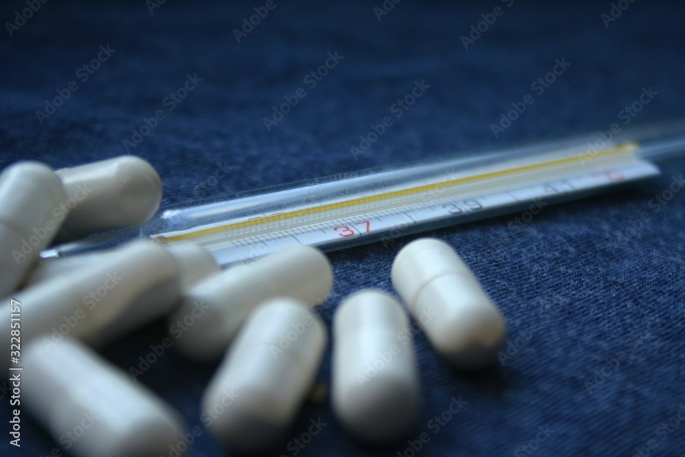 Tablets, pills and mercury thermometer on a blue background. Flu cold concept. Healthcare medical concept. Medicine pill. Emergency medical treatment. Tablets, pills and mercury thermometer on a blue background. Flu cold concept. Healthcare medical concept. Medicine pill. Emergency medical treatment.