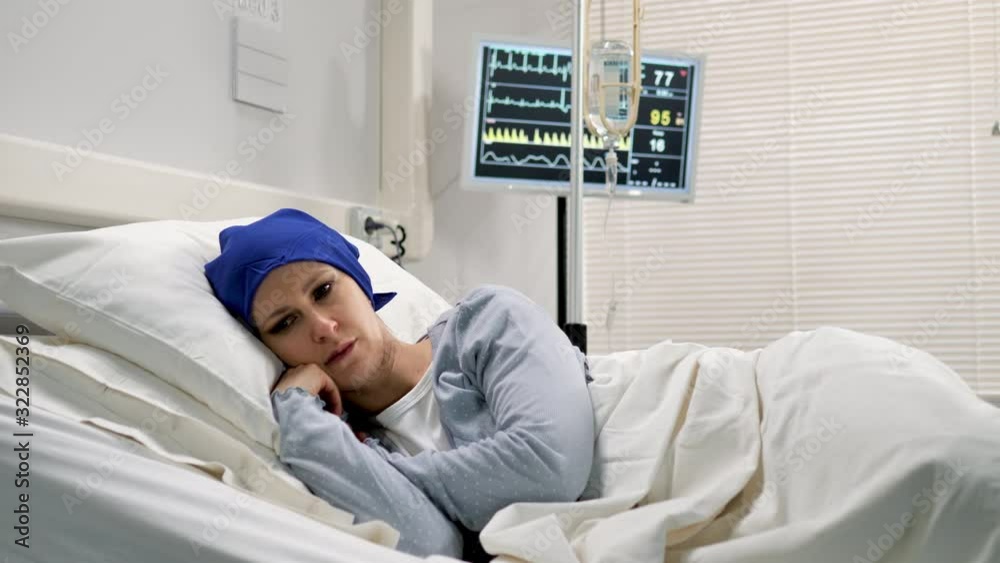 sad female cancer patient with hat lying unhappy in the hospital bed staring into space after the surgery sad female cancer patient with hat lying unhappy in the hospital bed staring into space after the surgery
