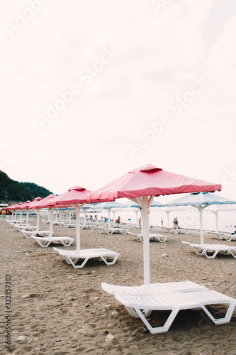 white sunbeds with colorful umbrellas on a pebble beach in the summer © Дарья Фомина