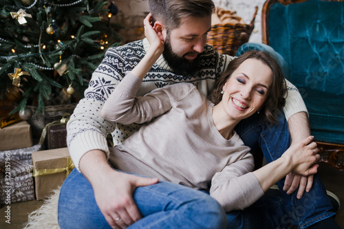 Winter weekend at home. Young caucasian couple in cozy sweaters hugging near the Christmas tree. Celebrating New Year, Valentine, love, romance concept.