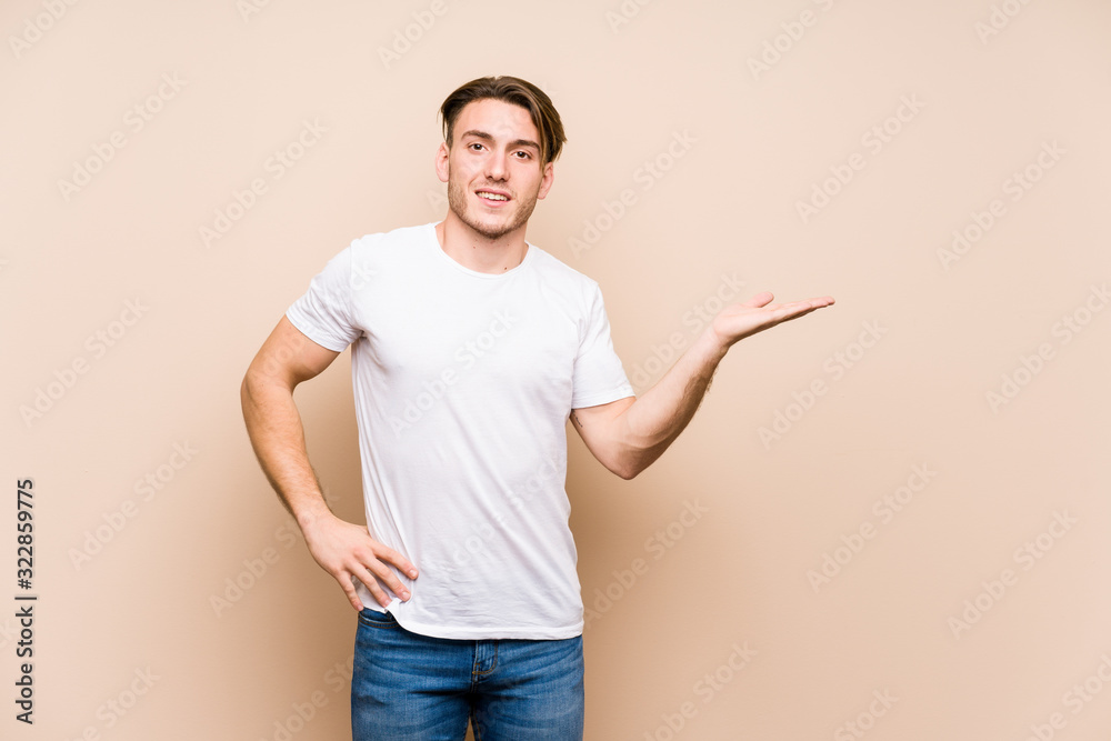 Young caucasian man posing isolated showing a copy space on a palm and holding another hand on waist. Young caucasian man posing isolated showing a copy space on a palm and holding another hand on waist.