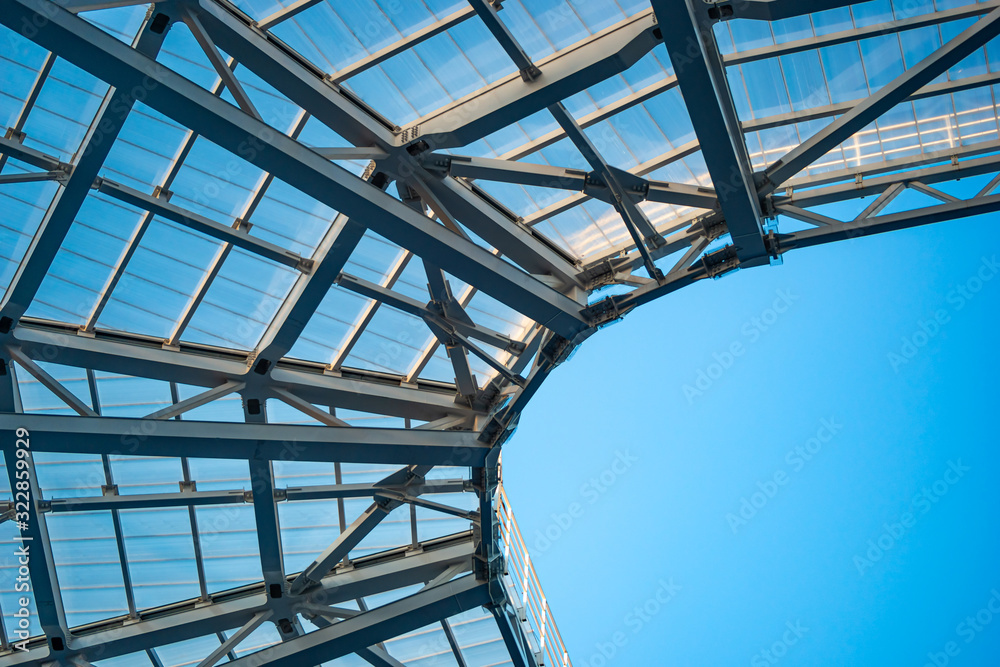 View of the roof of the sports stadium from the inside. Metal structures and glass ceilings are visible against the blue sky.