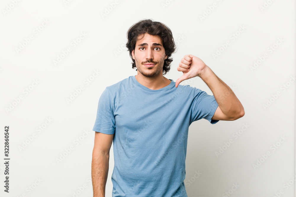Young handsome man against a white background showing a dislike gesture, thumbs down. Disagreement concept. Young handsome man against a white background showing a dislike gesture, thumbs down. Disagreement concept.