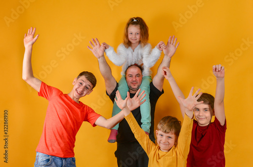 A father and four joyful children raised their hands up, a daughter sits on my father?s shoulders. Funny and funny beautiful children in colorful clothes. © andov