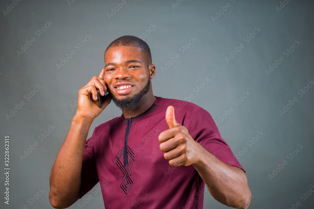 young handsome nigerian man isolated over grey background receiving a call from his smart phone young handsome nigerian man isolated over grey background receiving a call from his smart phone
