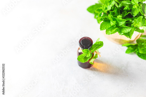 Oil of peppermint in small bottles, fresh green mint on white background. Selective focus, copy space photo