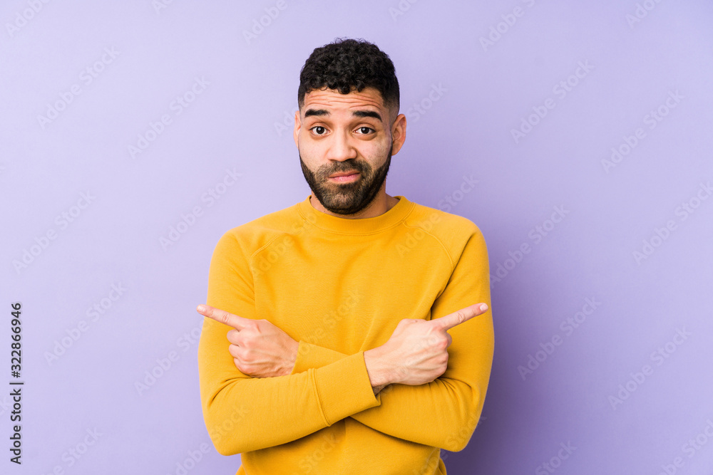 Young mixed race arabic man isolated points sideways, is trying to choose between two options. Young mixed race arabic man isolated points sideways, is trying to choose between two options.