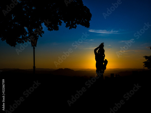 Silhouette of a statue during sunset with colorful clouds and blue sky and sun behind the sculpture