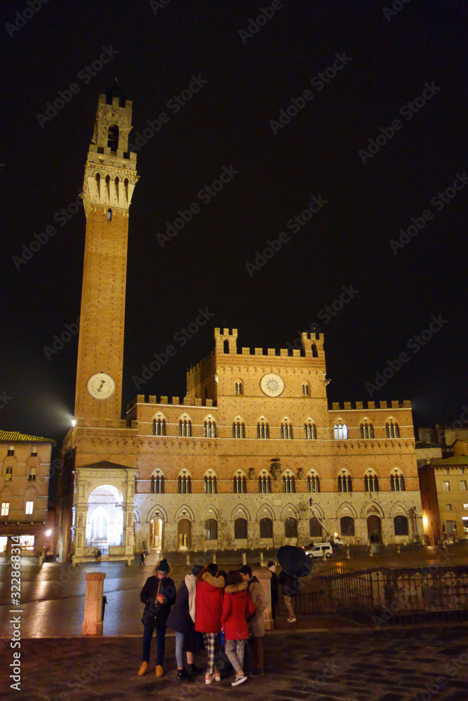 Siena by night. Piazza del Campo and Tower del Mangia illuminated..Tourists in the square.