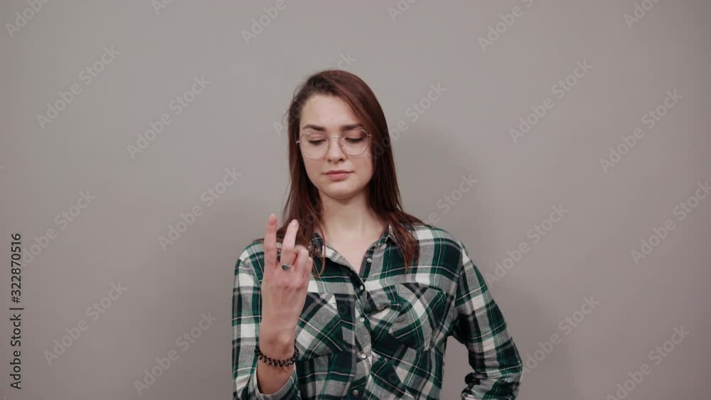 Young brunette girl blue green in checked shirt on grey background stylish woman in glasses surprised, shows four fingers Young brunette girl blue green in checked shirt on grey background stylish woman in glasses surprised, shows four fingers