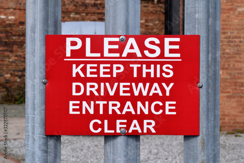 Red Metal Warning Sign on Steel Fence 'Please Keep This Driveway Entrance Clear' 