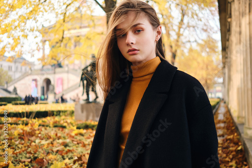 Beautiful stylish girl confidently looking in camera on beautiful autumn city street