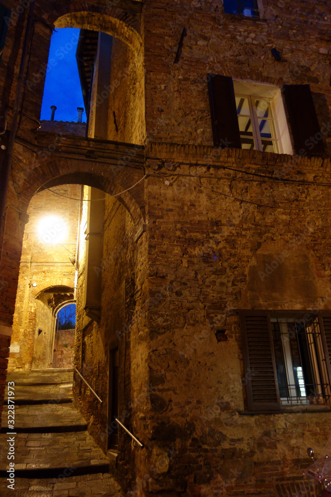 Siena by night. Small illuminated street in the center of Siena uphill with arches.