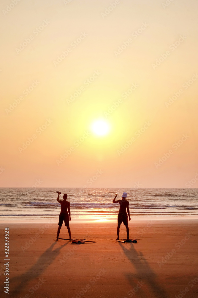 two unrecognizable men excerscising at sunset by holding small weights on a deserted beach