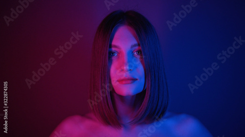 Lovely young woman with straight hair looking at camera. Amazing purple neon lightning. Shooting of attractive girl with blue eyes. Look. Beautiful Caucasian model. Colourful.