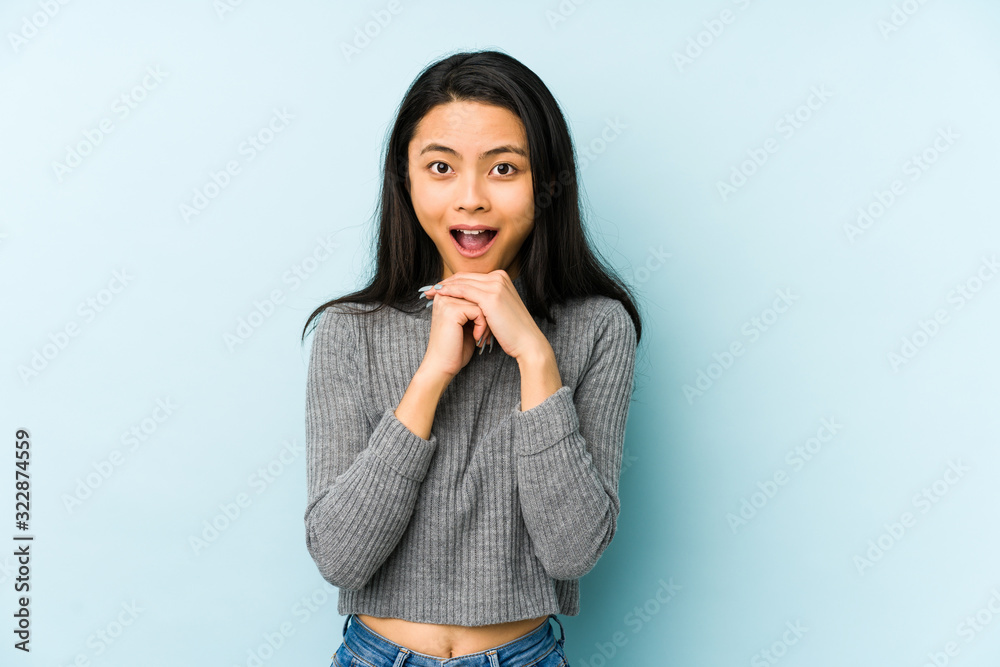 Young chinese woman isolated on a blue background praying for luck, amazed and opening mouth looking to front. Young chinese woman isolated on a blue background praying for luck, amazed and opening mouth looking to front.