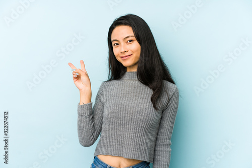 Young chinese woman isolated on a blue background joyful and carefree showing a peace symbol with fingers.