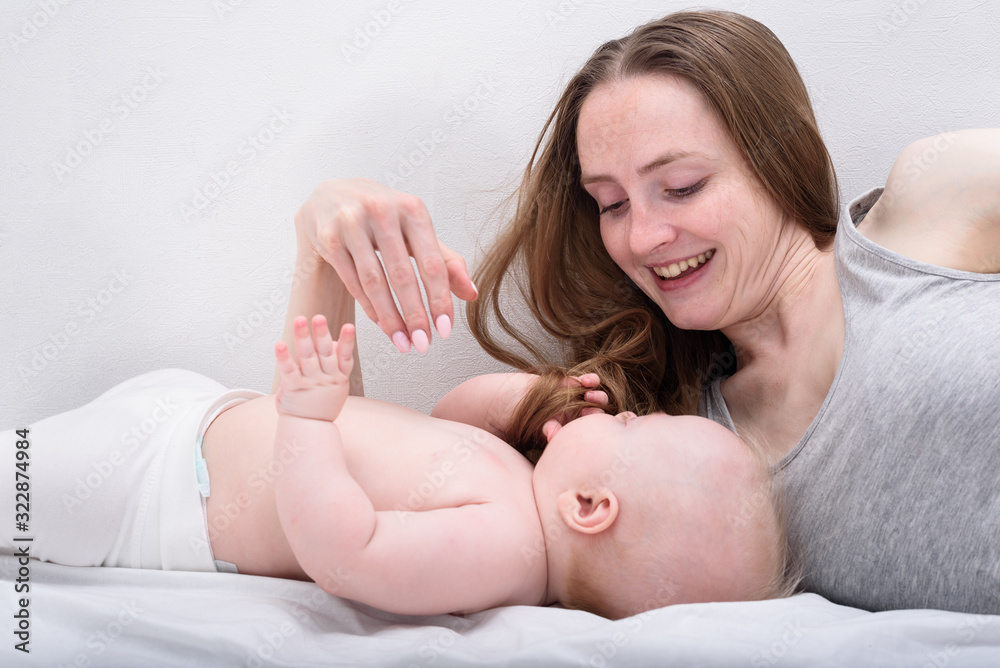 Young mother smiles and plays with baby. Happy motherhood parenthood concept Young mother smiles and plays with baby. Happy motherhood parenthood concept