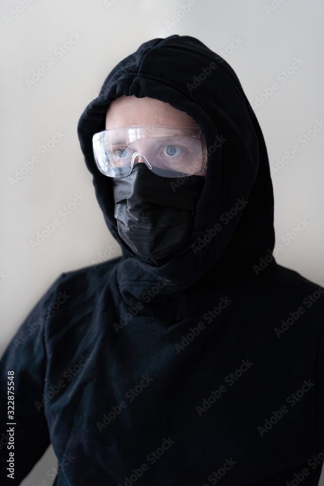 Portrait of a man protected from coronavirus with a medical mask and glasses, dressed in black clothes on a light background. Flu pandemic covid 19