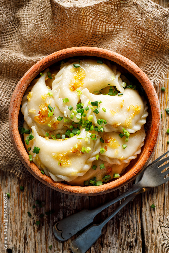 A top view of a bowl with traditional vegetarian dumplings stuffed with curd cheese, potatoes, onions and spices on a rustic wooden table. A top view of a bowl with traditional vegetarian dumplings stuffed with curd cheese, potatoes, onions and spices on a rustic wooden table.