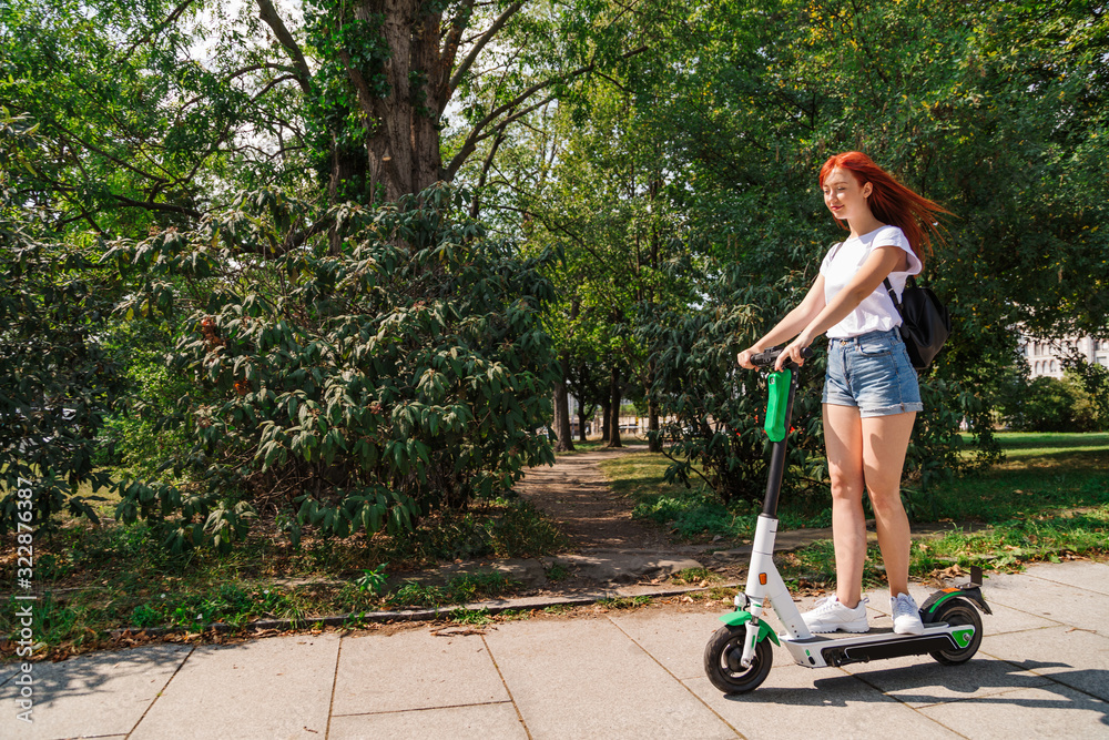 Naklejka premium Woman rides on electric scooter along sunny street