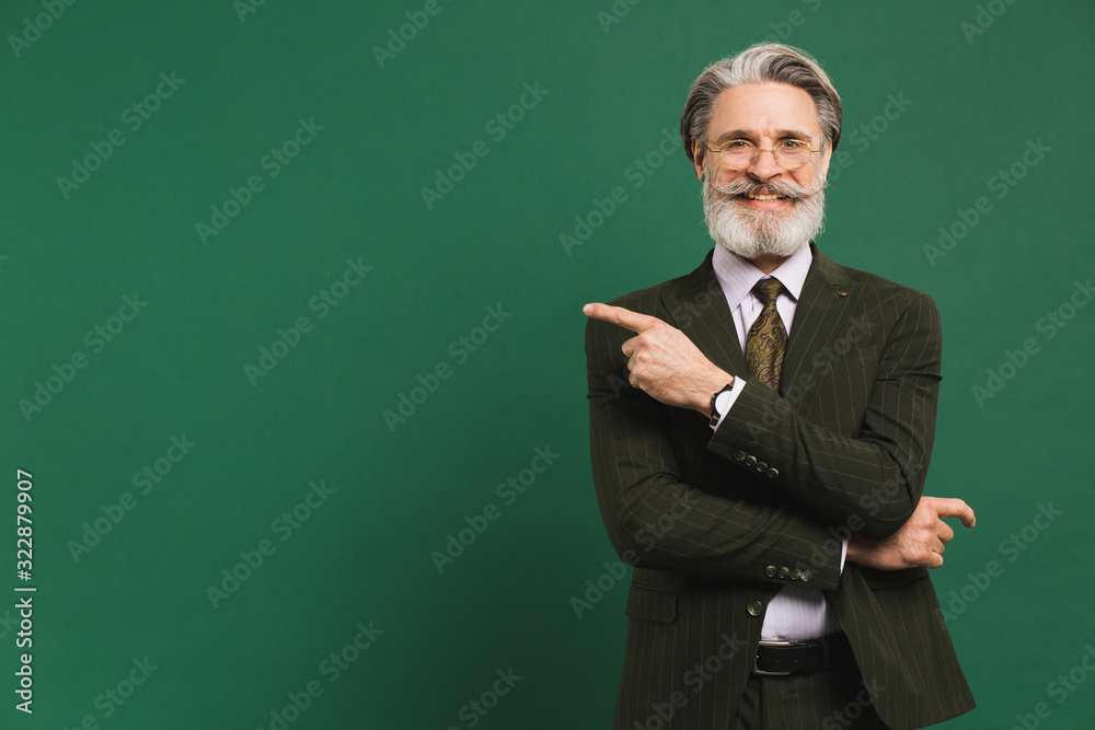 Stylish bearded middle-aged man in the khaki suit shows on the copy space of green background Stylish bearded middle-aged man in the khaki suit shows on the copy space of green background