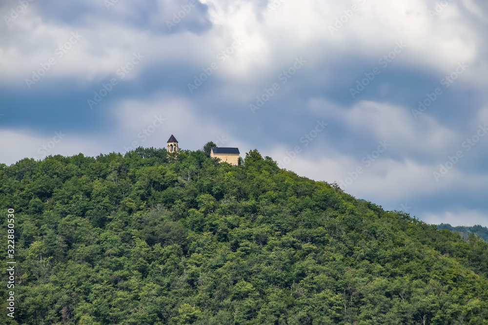 Remote church in foothills of Caucasus Mountains in Georgia where you only see tower tiny on top of the hill among all the trees near Sachkhere