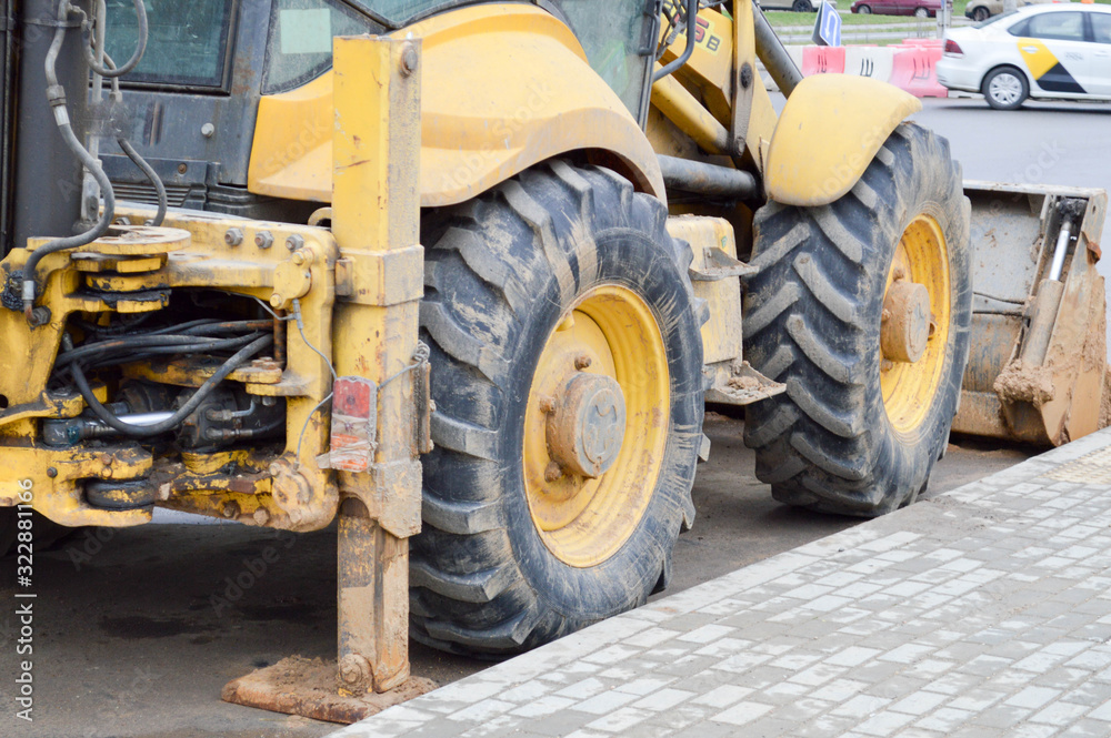 Obraz premium Big bright yellow powerful industrial heavy excavator tractor, bulldozer, specialized construction equipment for road repair during the construction of a new micro-district in a big city